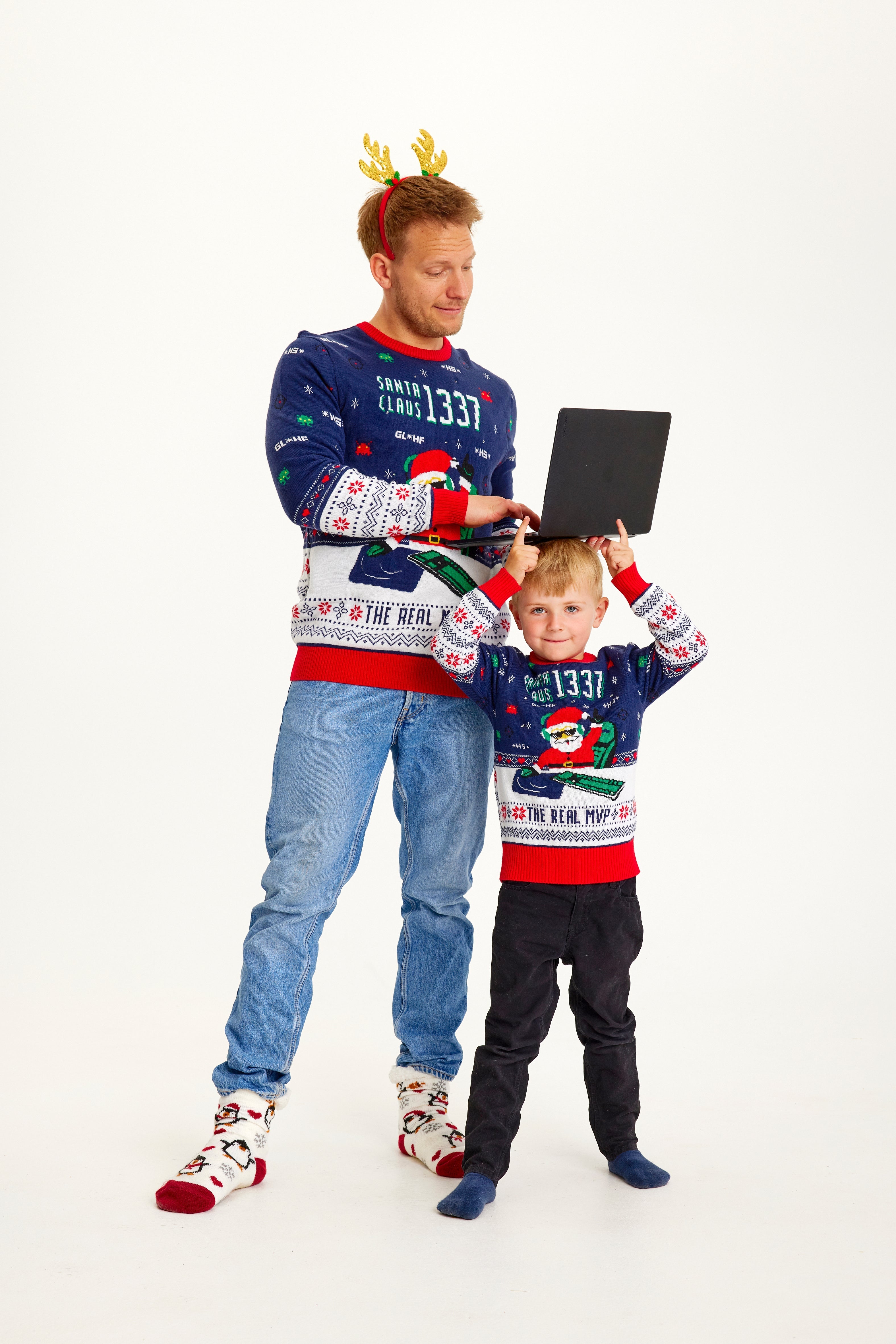 Et barn og en mann poserer sammen iført en blå julegenser med julenisse og lys på.